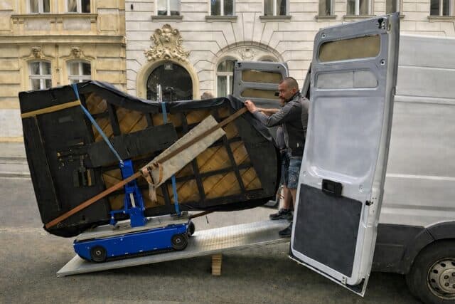 Piano Shift Team verlädt gesichertes Klavier mit motorisiertem Klavierroller über eine Rampe in den Transporter